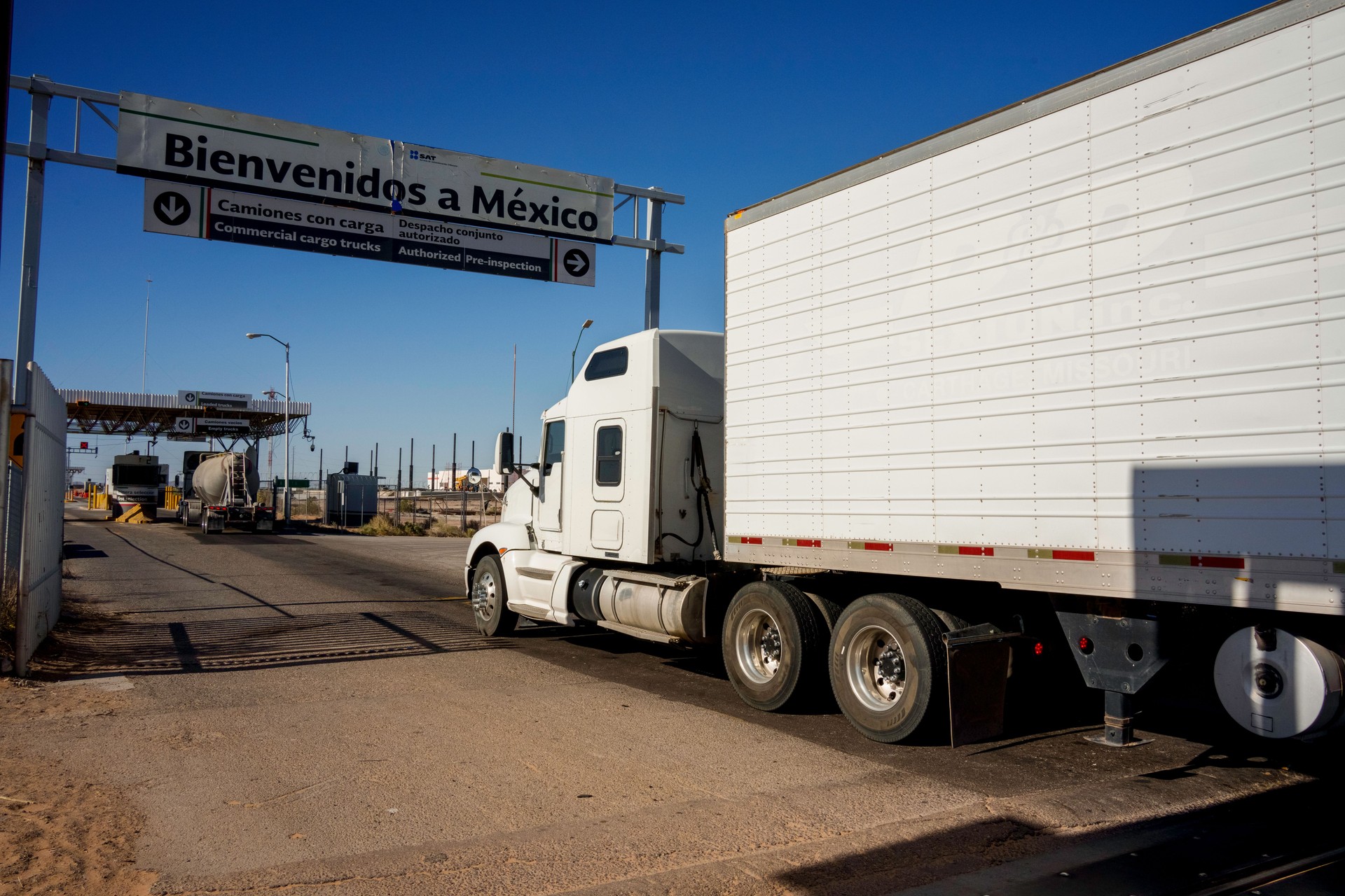 White Semi Truck Crossing the International Border Barrier Between the United States and Mexico Transporting Commercial Cargo